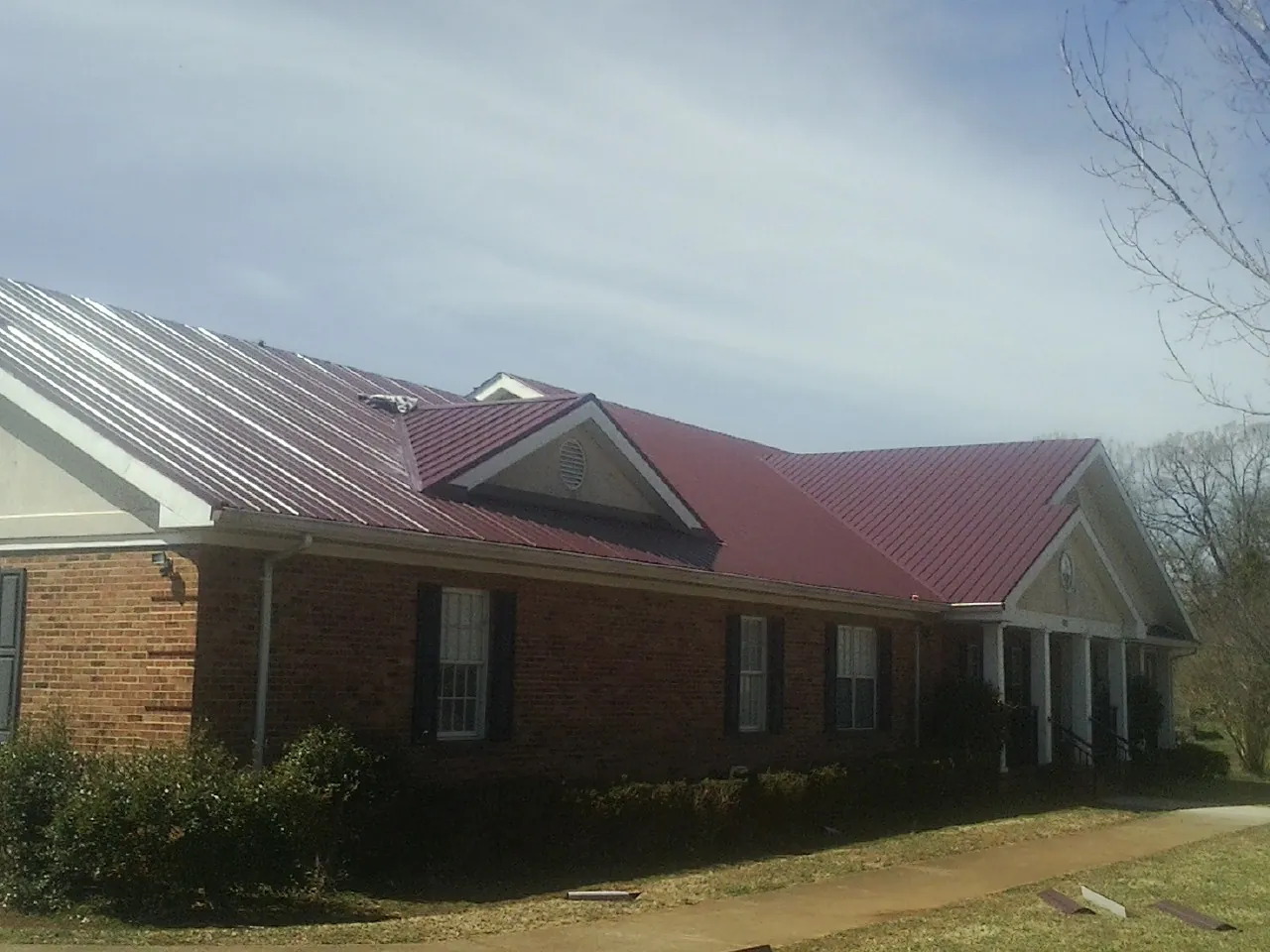 Red metal roof with gabled entries on a long brick building, from a Hail Damage Roof Repair job in Evans