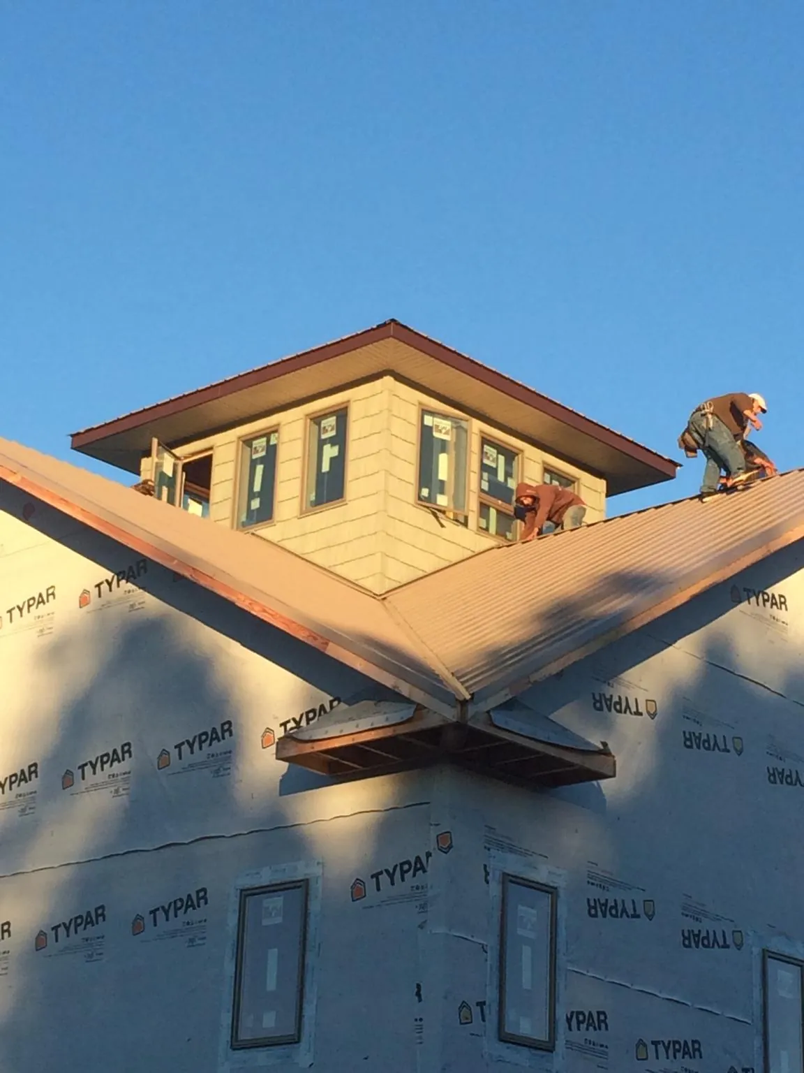 Roofers working around a rooftop cupola on a new metal roof at sunset — Roof Waterproofing in Evans by Roofing Brothers